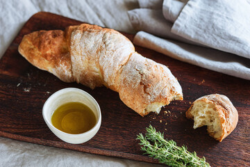 Artisan sourdough bread served with olive oil and thyme on wooden cutting board. Selective focus