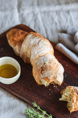 Artisan sourdough bread served with olive oil and thyme on wooden cutting board. Selective focus