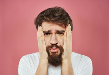 bearded man in a white t-shirt hand gestures anger pink background