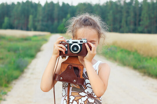 Happy beautiful  little girl in retro outfit  is taking pictures with old film camera.