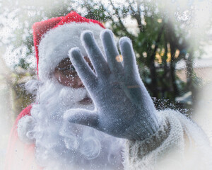The hand of Santa Claus wipes the glass of the window. Shot from the house.