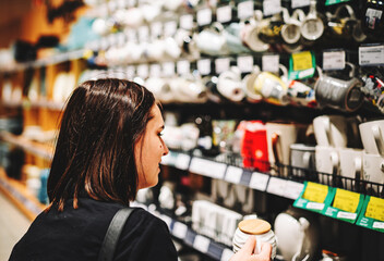 Shopping yong woman looking at the shelves with cup in supermarket.