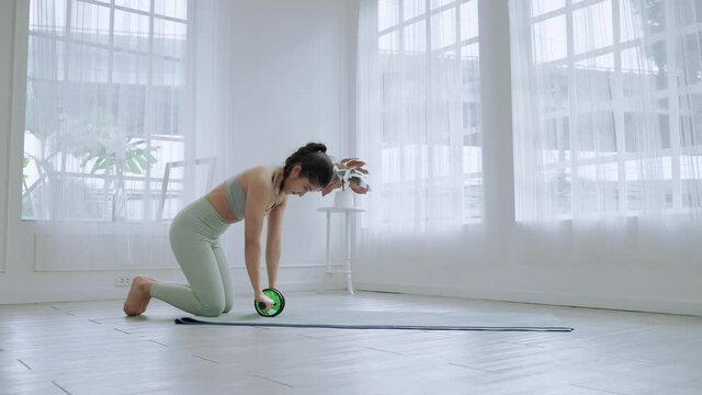Asian Sporty Woman is using Roller abs wheel exercise machine to build abdominal and back muscles, fitness concept and wellness.
