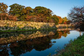 Amazing autumn trees reflected in castle moat in late afternoon, golden light, blue sky.