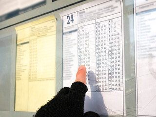 Man checking the bus or tram timetable pointing his finger on the arrival departure hours table....