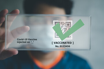 Man wears mask holding digital tag with details of his covid-19 vaccination.