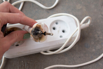 the hand pulling the plug out of the burnt outlet short circuit
