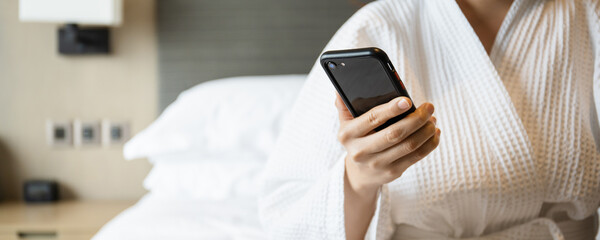 Unrecognizable Asian young woman in bathrobe or shower suit using a smartphone.