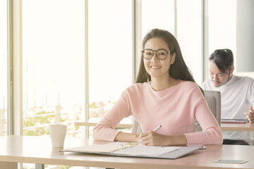 Asian business woman who sitting work by notebook in feeling happy at the office with daylight from window and blur garden background.