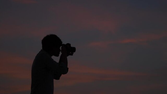 Silhouette of an Indian photographer taking photos with his camera during the sunset. Man taking pictures with his camera during the sunset. Photographer takes out his camera and takes photo.	