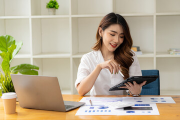 Smiling Asian businesswoman working on laptop in the office sitting at a desk in room Finance...