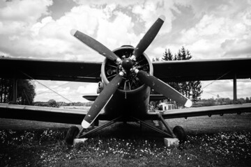  old vintage war airplane, cloudy spring day, young grass and dandelions under the plane. biplane with propeller. Black and white monochrome close up of old military machine	
