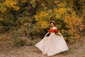 Fototapeta premium a woman in a beautiful dress in a brown hat in the fall against the background of yellow leaves.free space for text