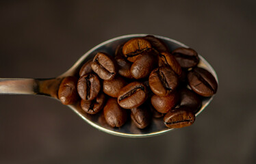 Fototapeta premium A spoon filled with roasted coffee beans on a dark background. Concept: export and import of coffee beans, coffee consumption.