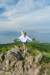 Obraz premium Girl in summer clothes on the top of the mountain near the sea