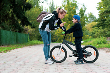 A little boy on a bicycle in the park listens to his mother, who explains to him that he can not go on the road where cars go, and ride only on bike paths