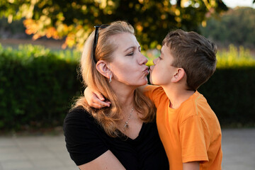 Mom and little son hug in the park and mom kisses son, they reconciled after a quarrel, misunderstanding and now communicate with joy - Powered by Adobe