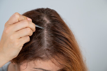 Caucasian woman finds gray hair and removes it with tweezers. Signs of aging.