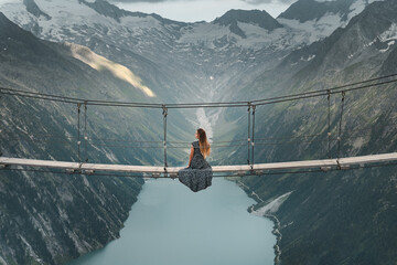 Young woman in beautiful dress sitting on a suspended bridge near Olperer Hütte