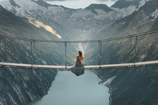 Young woman in beautiful dress sitting on a suspended bridge near Olperer H&uuml;tte