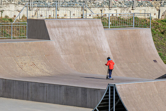 A boy rides a scooter at a skateboarding stadium