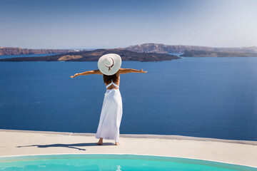 A woman in a white dress and sunhat stands by the pool and enjoys the beautiful view over the...