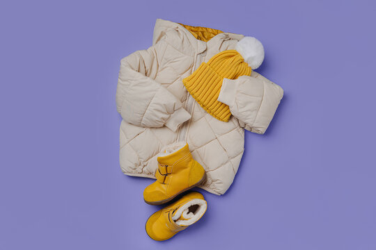 Kids Warm Puffer Jacket With Yellow  Hat And Boots On Blue Background. Stylish Childrens Outerwear. Winter Fashion Outfit