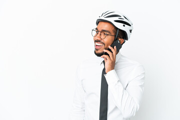 Young business latin man holding a bike helmet isolated on white background keeping a conversation with the mobile phone with someone