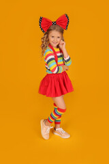 beautiful happy blonde girl with a red bow on her head in a red skirt, a colored blouse with colored socks on a yellow background