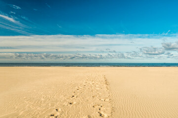Fototapeta na wymiar Large, empty beach with fine white sand over blue sky in in Liepaja, Latvia. Footprints in the sand leading to to sea. Latvian landscape captured in a sunny autumn day. Popular holiday destination. 