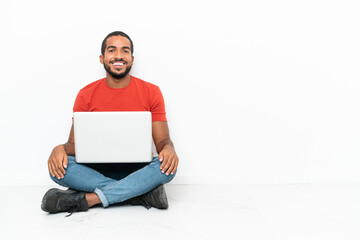 Young Ecuadorian man with a laptop sitting on the floor isolated on white background laughing