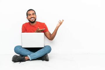 Young Ecuadorian man with a laptop sitting on the floor isolated on white background extending hands to the side for inviting to come