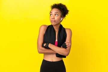 Young African sport woman isolated on yellow background making doubts gesture while lifting the...