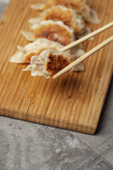 Gyoza or dumplings snack with soy sauce on wood board and grey clay background. Using chopsticks