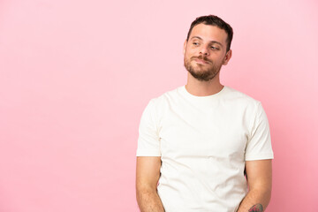Young Brazilian man isolated on pink background having doubts while looking side