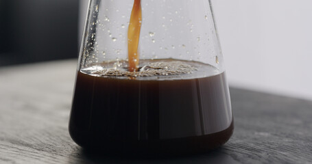 coffee pour into glass carafe on black oak table