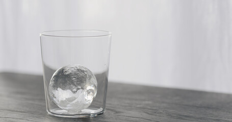 clear ice ball in tumbler glass on black oak table