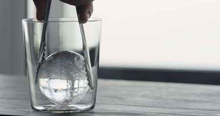 man put clear ice ball in tumbler glass on black oak table