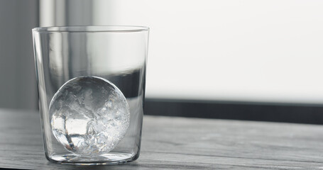 clear ice ball in tumbler glass on black oak table