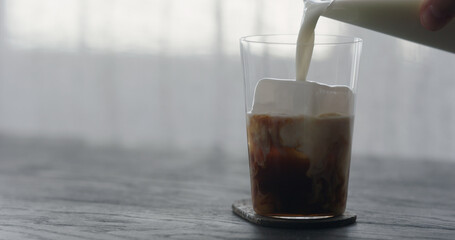 pour milk into ice coffee on black wood table