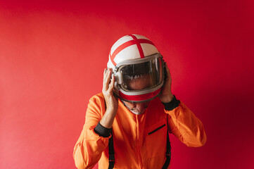 Astronaut with an orange space suit taking off his helmet on a red background - Powered by Adobe