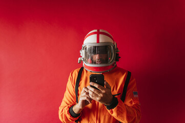 Astronaut with a helmet and an orange space suit scrolling on his phone on a red background