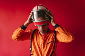 Astronaut with an orange space suit taking off his helmet on a red background