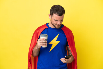 Super Hero Brazilian man isolated on yellow background holding coffee to take away and a mobile