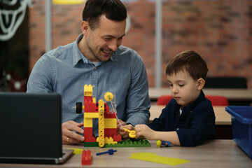 4 years old kid and his father making red yellow toy robot together. Man assembling a robot for his son. Fathers day