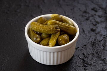 Crunchy pickled cornichons in a white ceramic bowl. Marinated green gherkins. Pickled cucumber. Delicious baby pickles. Tasty canned vegetables