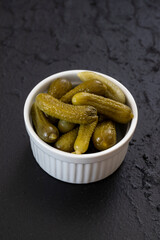 Crunchy pickled cornichons in a white ceramic bowl. Marinated green gherkins. Pickled cucumber. Delicious baby pickles. Tasty canned vegetables