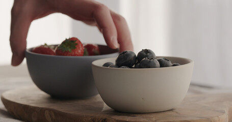 man put fresh strawberries and blueberries in bowls on olive wood board