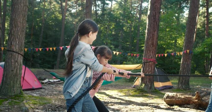 Full length view of the group of elementary school children enjoyed tug of war together at the camp at the forest. People having outdoor activities concept