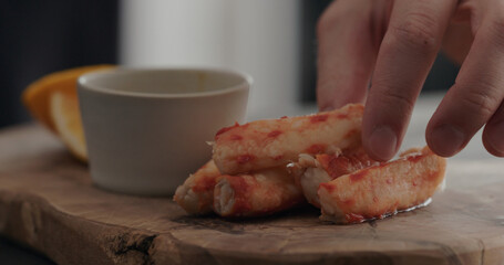 man take crab leg from olive wood board